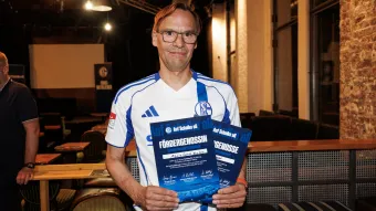 Schalke-Mitglied hält Urkunde der Genossenschaft hoch